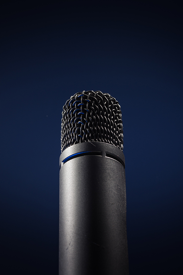 Dark blue background with modern gray to black microphone in foreground.