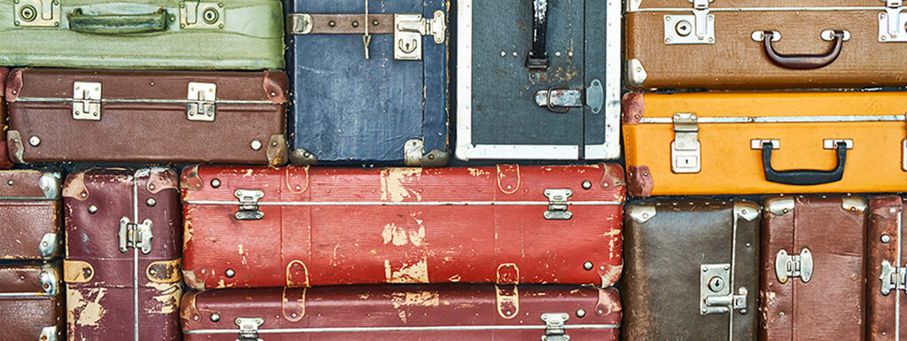 Multicolored old suitcases are stacked and fill the entire frame. At the bottom is the word ARTIFACTS in black across the entire span of the image