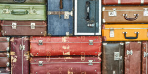 Multicolored old suitcases are stacked and fill the entire frame. At the bottom is the word ARTIFACTS in black across the entire span of the image