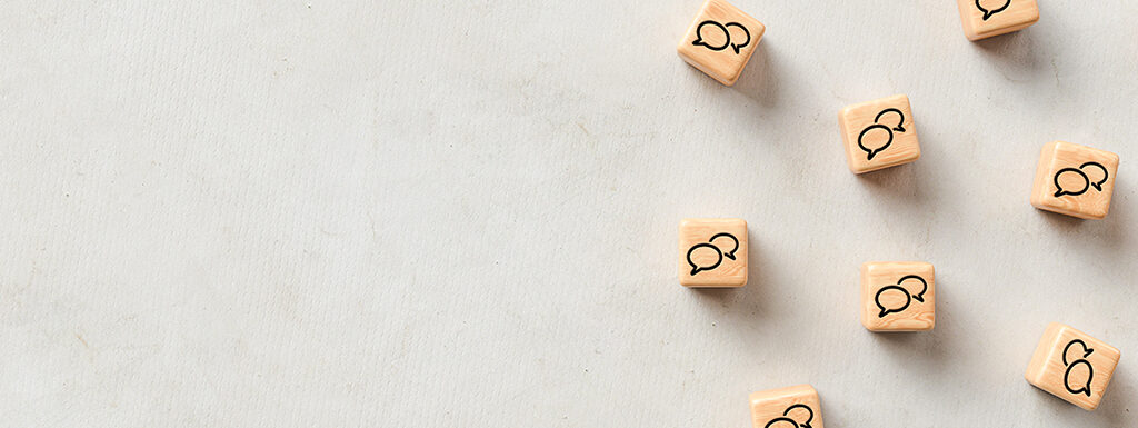 Light background that is colored like cement with small light brown wooden cubes, like dice, on the right hand side with chat icons or speech bubbles on each cube